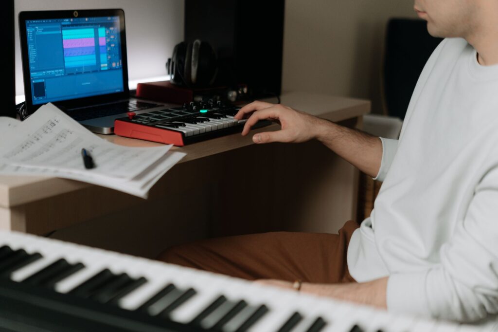 Persona transformando recuerdos personales en una canción, escribiendo letras en un diario junto a un piano con fotos antiguas.