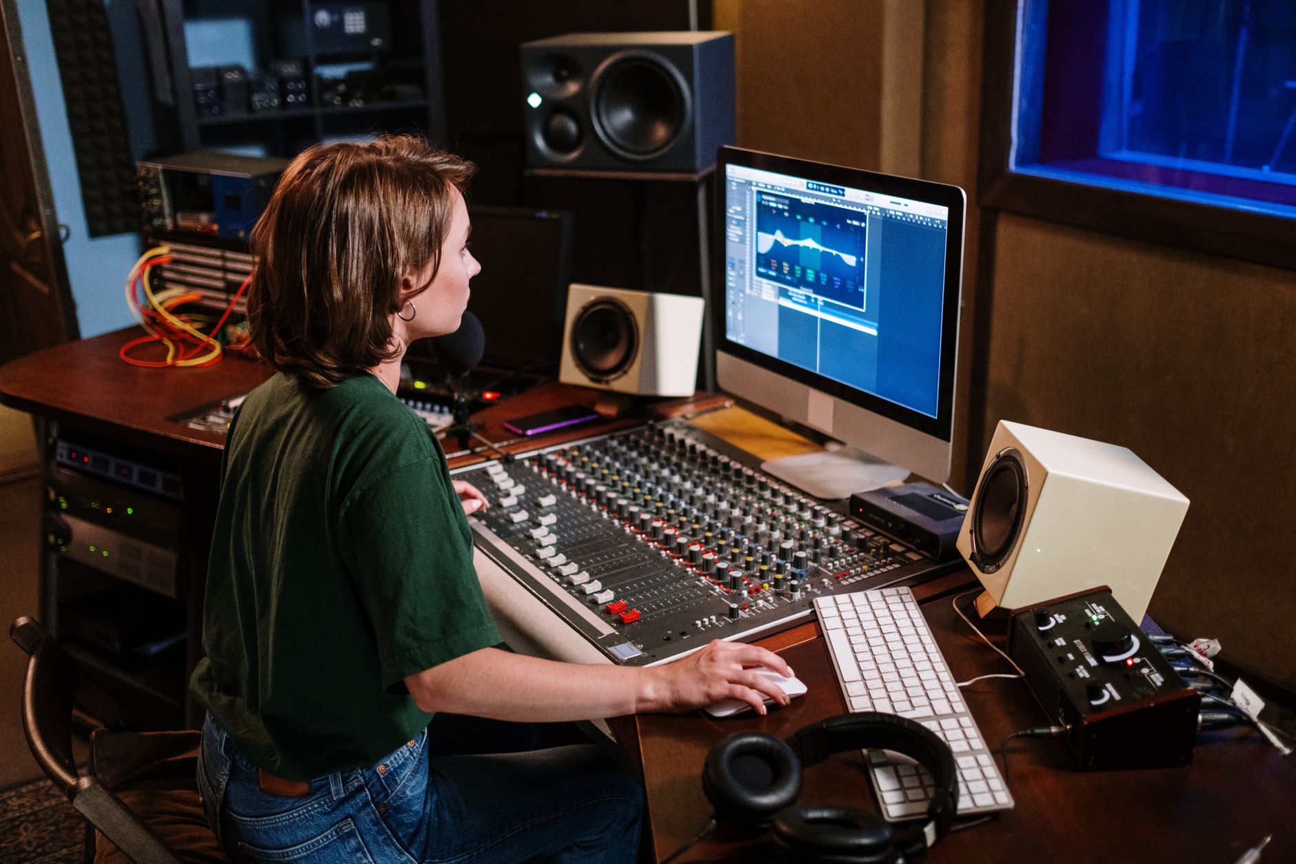 Ingeniero de audio concentrado en un estudio, usando audífonos y monitores de estudio para mezclar música.