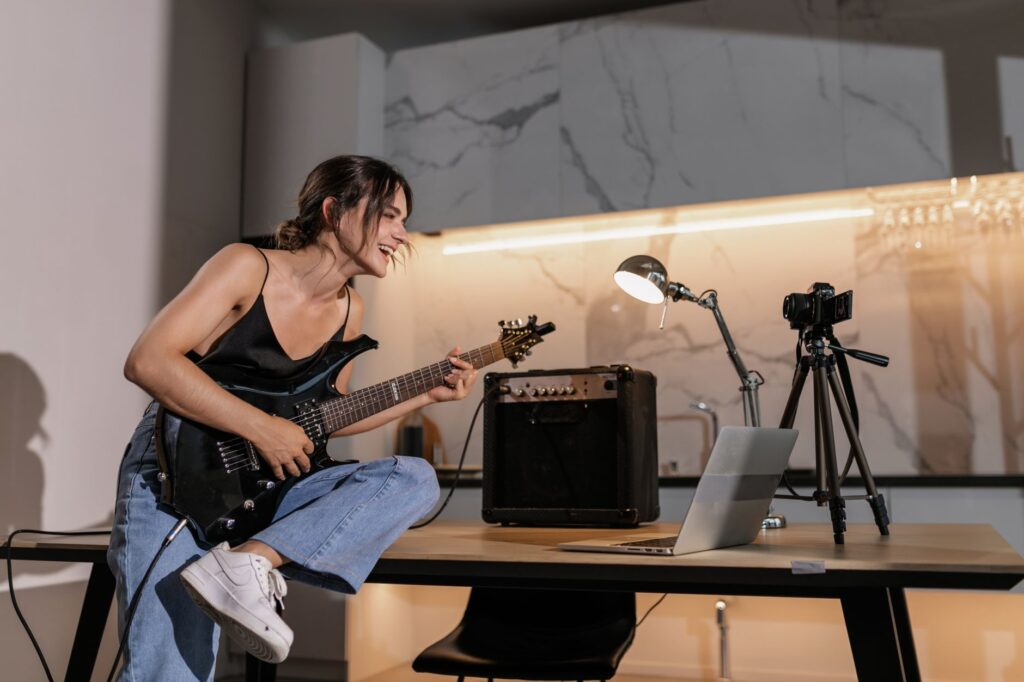 Músico independiente concentrado produciendo música en su estudio casero con laptop y equipo de audio.